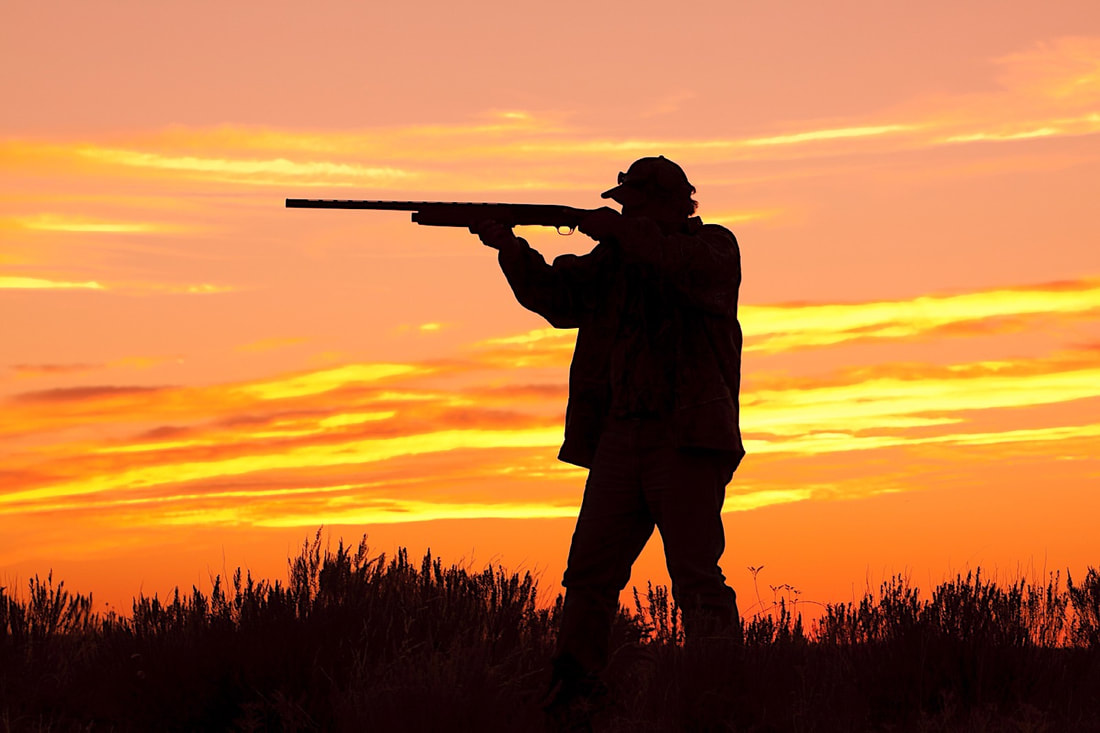 Silhouette of man with hunting rifle against a sunset.